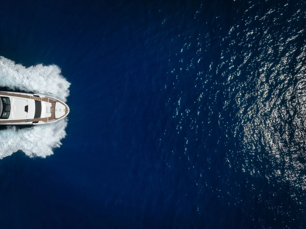 A white motor yacht seen from above, running through deep blue open water